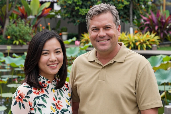 Steven and Linh smiling in a lush Vietnamese garden with lotus pond
